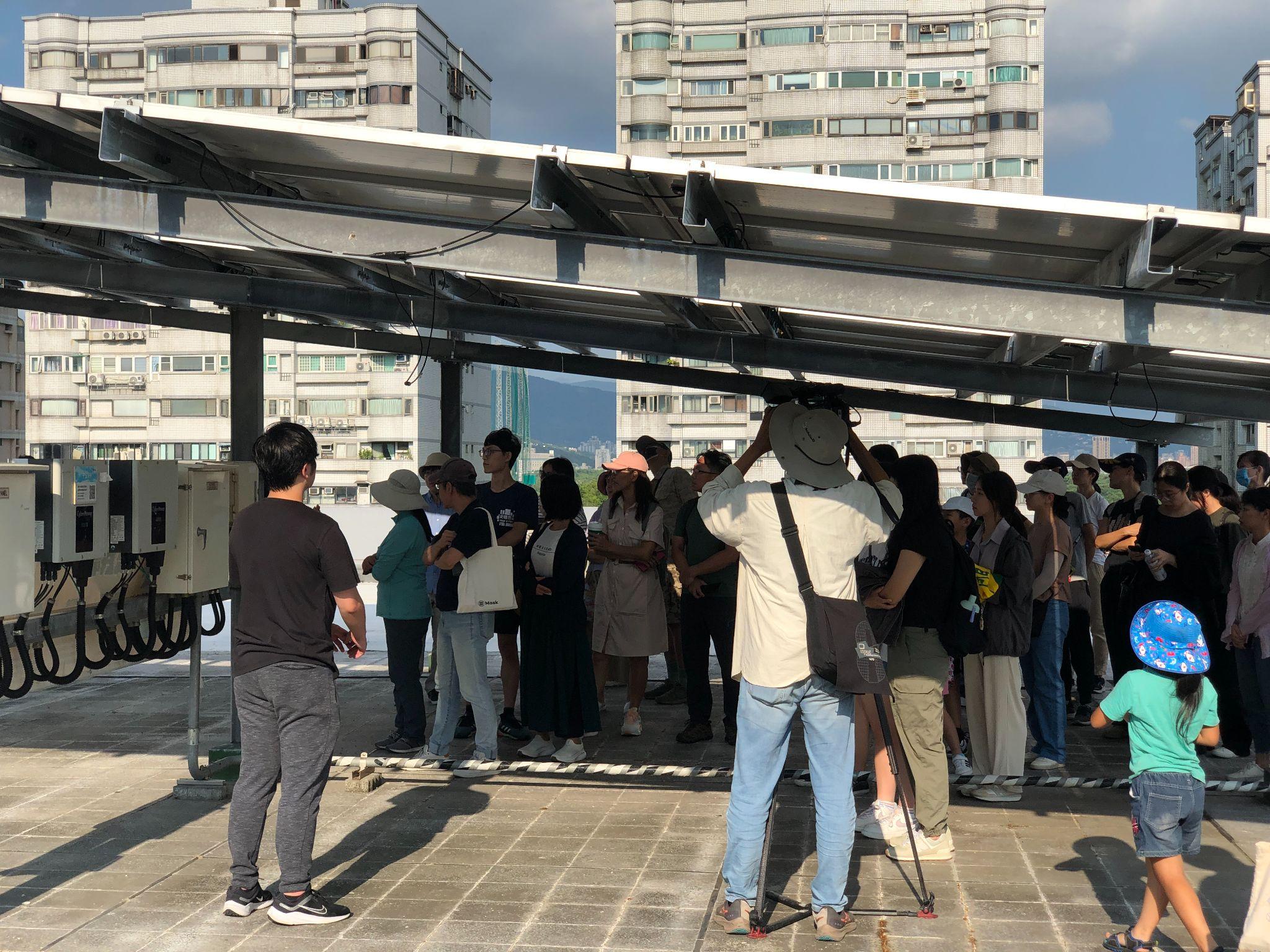 市民參訪由主婦聯盟環境保護基金會與北投在地24位市民廠長共同出資成立的社區公民電廠「干豆好公民電廠」，躲在太陽能板下避暑。
